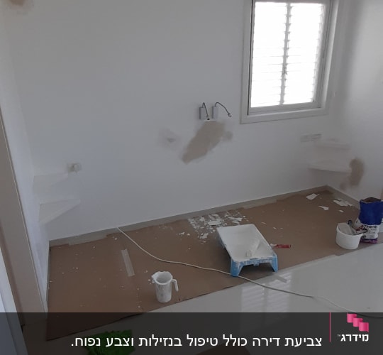 חדר עם קירות צבועים, כלי עבודה וצבע על הרצפה